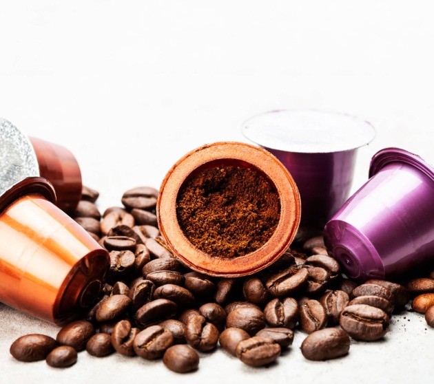 Open Espresso coffee capsule with grounded coffee inside, assorted coffee pods and roasted coffee beans on grey background